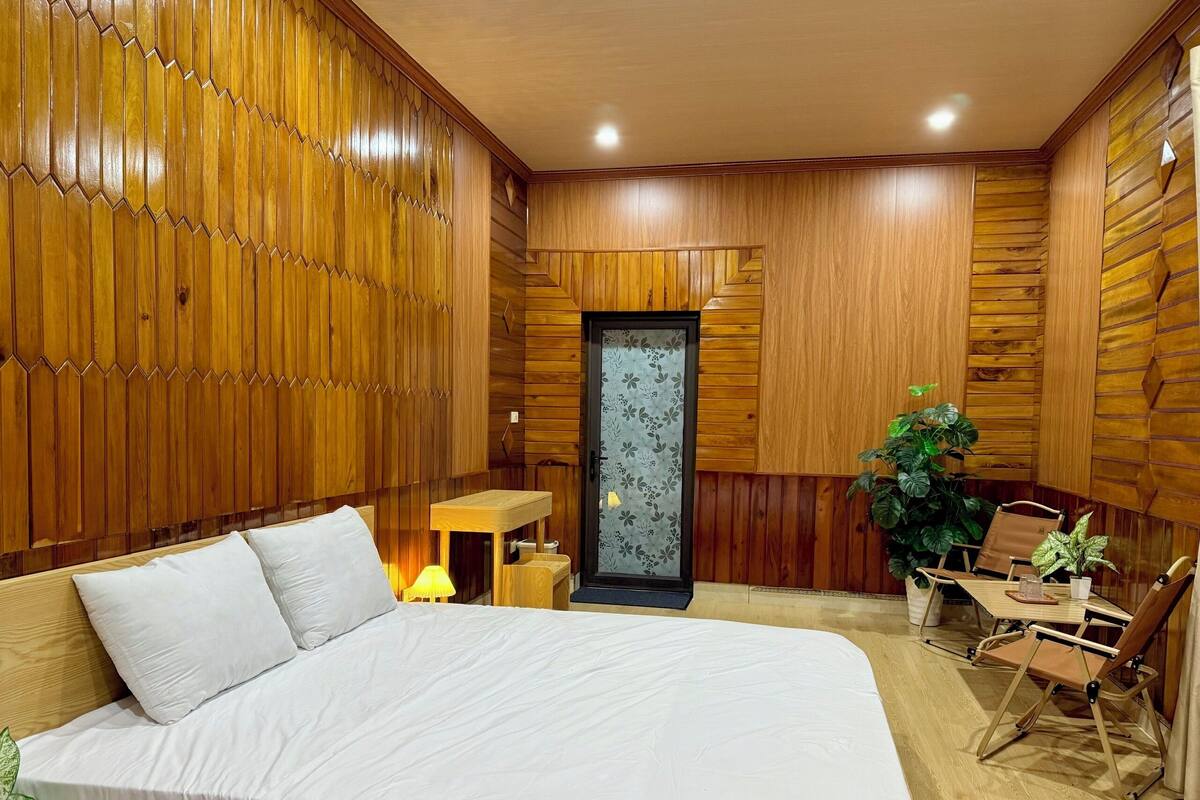 Ein Zimmer mit einem großen Bett, Holzwandverkleidung, einem kleinen Tisch mit einer Lampe und einem Sessel.
