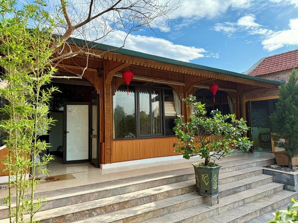 A traditional wooden building with a tiled roof, a staircase leading to the entrance, and a potted plant on the steps. - May Garden Homestay (Hoa Lu)