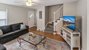 Ein Wohnzimmer mit Sofa, Couchtisch, Fernseher, Treppe und Deckenventilator.
