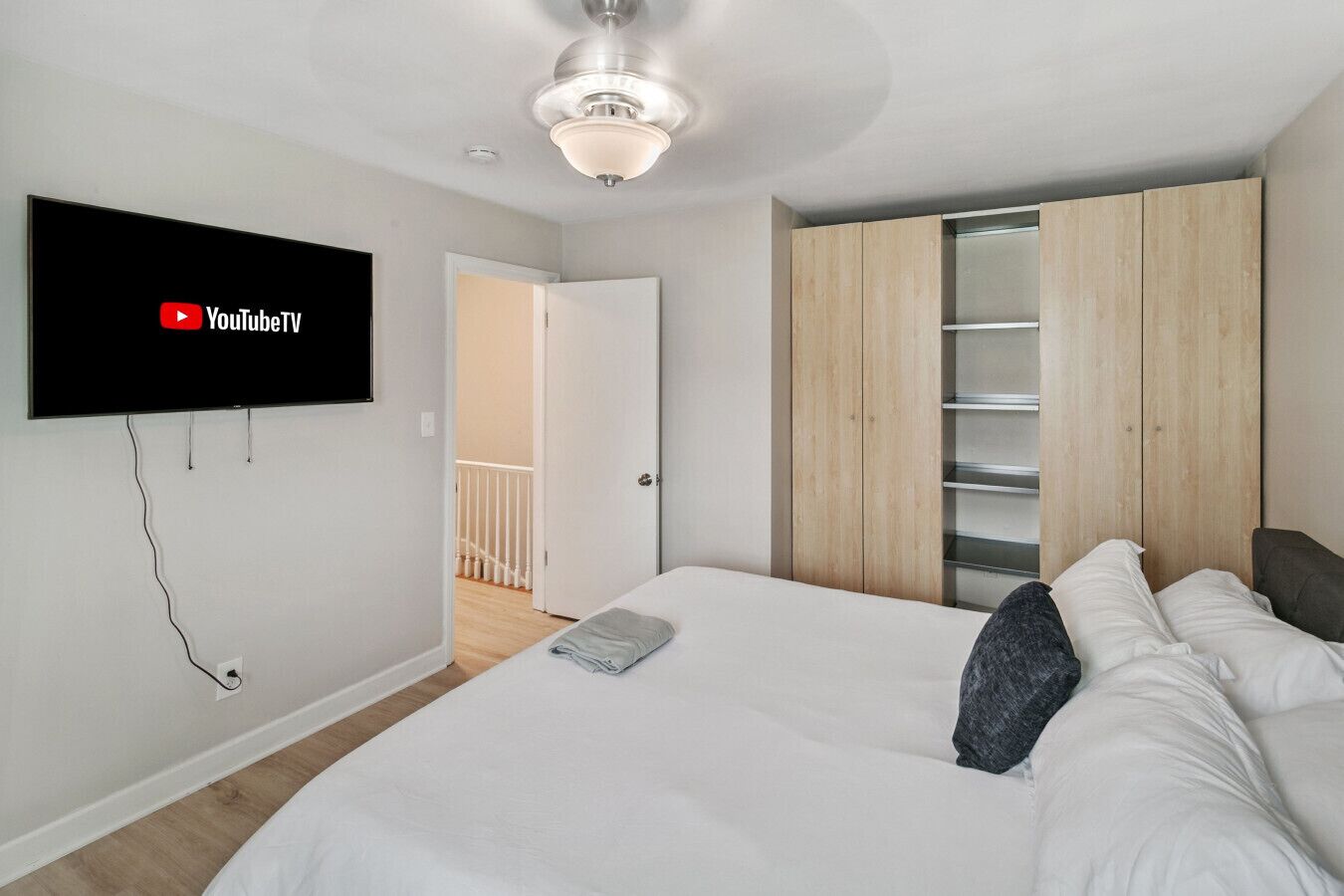 Un dormitorio con una cama, un televisor montado en la pared, un armario y un ventilador de techo.