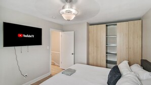 Ein Schlafzimmer mit einem Bett, einem an der Wand montierten Fernseher, einem Kleiderschrank und einem Deckenventilator.