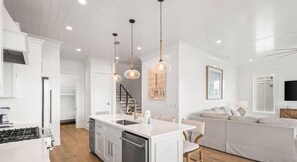 A modern kitchen with white cabinetry, a central island, pendant lighting, and a staircase leading to a loft.