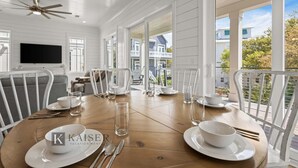 Een eetruimte met een houten tafel voor vier personen, witte stoelen en een plafondventilator.