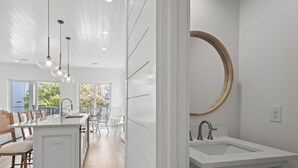 Een moderne keuken met een centraal eiland, witte kasten en hangende lampen.