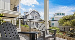 A balcony with two Adirondack chairs, a view of a two-story house with a balcony, and a wooden fence.