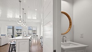 Una cocina moderna con una isla central, iluminación colgante y un amplio ventanal con vistas a un balcón.