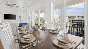 Comedor con mesa de madera dispuesta para cuatro, sillas blancas y un ventilador de techo.