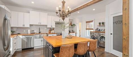 A kitchen with white cabinets, a wooden island, and bar stools.