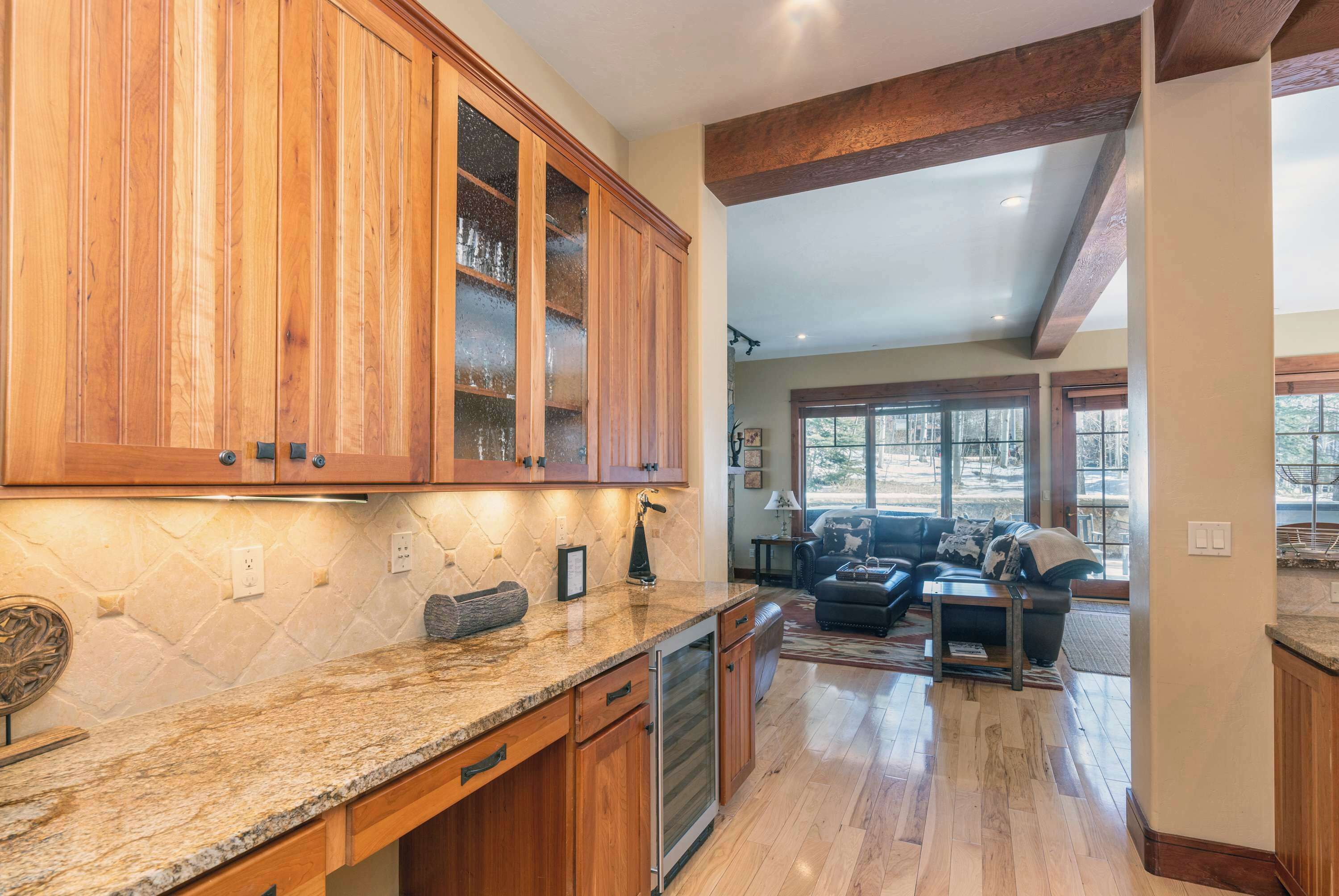 A spacious kitchen with wooden cabinets and granite countertops, leading to a living area with a fireplace and a view of the outdoors.