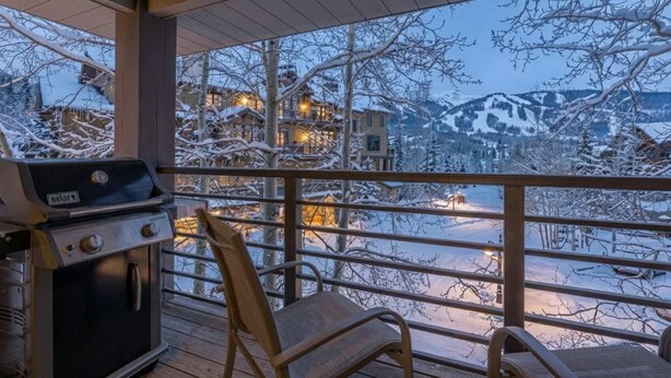 A balcony with a grill and chairs overlooking a snowy mountain landscape.
