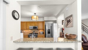 A kitchen with granite countertops, wooden cabinets, stainless steel appliances, and a bar area with stools.