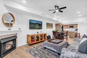 A modern living room with a fireplace, a dining area, and a kitchen.