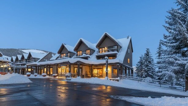 A multi-story lodge with a snow-covered roof and a well-lit entrance.