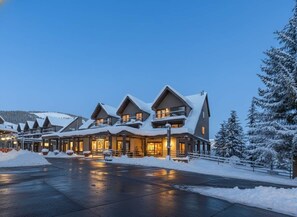 Un chalet à plusieurs étages, dont le toit est recouvert de neige et l’entrée est bien éclairée.