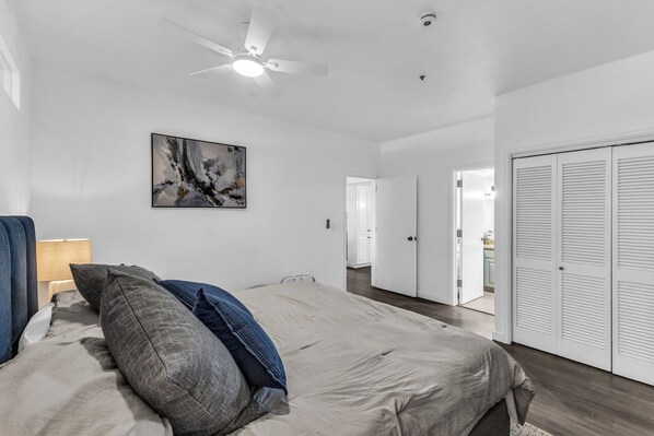 Une chambre à coucher avec un lit, un ventilateur de plafond, un tableau et une armoire.