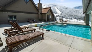 A pool area with lounge chairs, a pool, and a view of a snow-covered mountain.