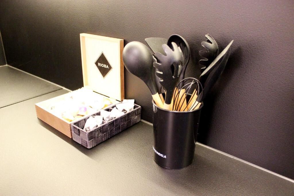 A kitchen area with a black utensil holder containing various kitchen tools, a box of paper towels, and a framed item on the wall.