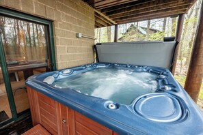 Ein Whirlpool mit Holzverkleidung und Metallrahmen, draußen gelegen mit Blick auf Bäume und ein Gebäude im Hintergrund.