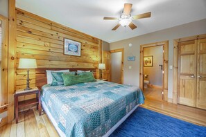 Ein Schlafzimmer mit einem Holzkopfende, einem Bett mit gesteppter Decke, zwei Nachttischlampen, einem Deckenventilator und einem blauen Teppich.