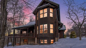Une cabane en bois dotée de nombreuses fenêtres et d’un balcon, entourée d’arbres et de neige.