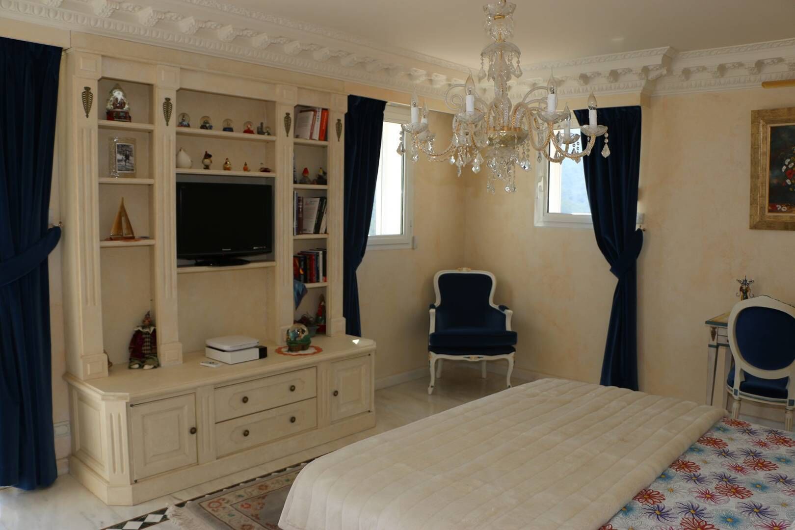 A bedroom with a large bed, a TV on a cabinet, a chandelier, and a chair.