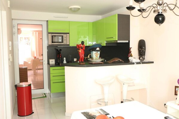 A modern kitchen with green cabinets, a microwave, and a sink. There is a dining area with a table and chairs.