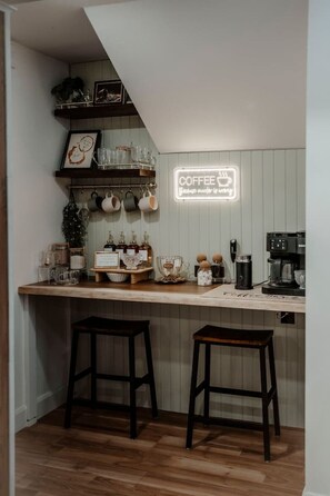 Eine gemütliche Küche mit einer Holzausziehtafel, zwei Barhocker, einer Kaffeemaschine und einem Neonlichtschild.