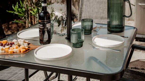 Een tafel met glazen blad buiten, met borden, een fles en glazen.