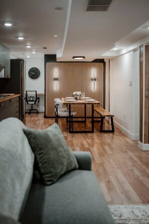 Ein modernes Wohnzimmer mit einer Couch, einem Esstisch mit Stühlen und einer Küchenzeile im Hintergrund.