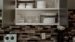 Een keuken met open kastjes, daarin witte servies, glazen en een koffieapparaat.