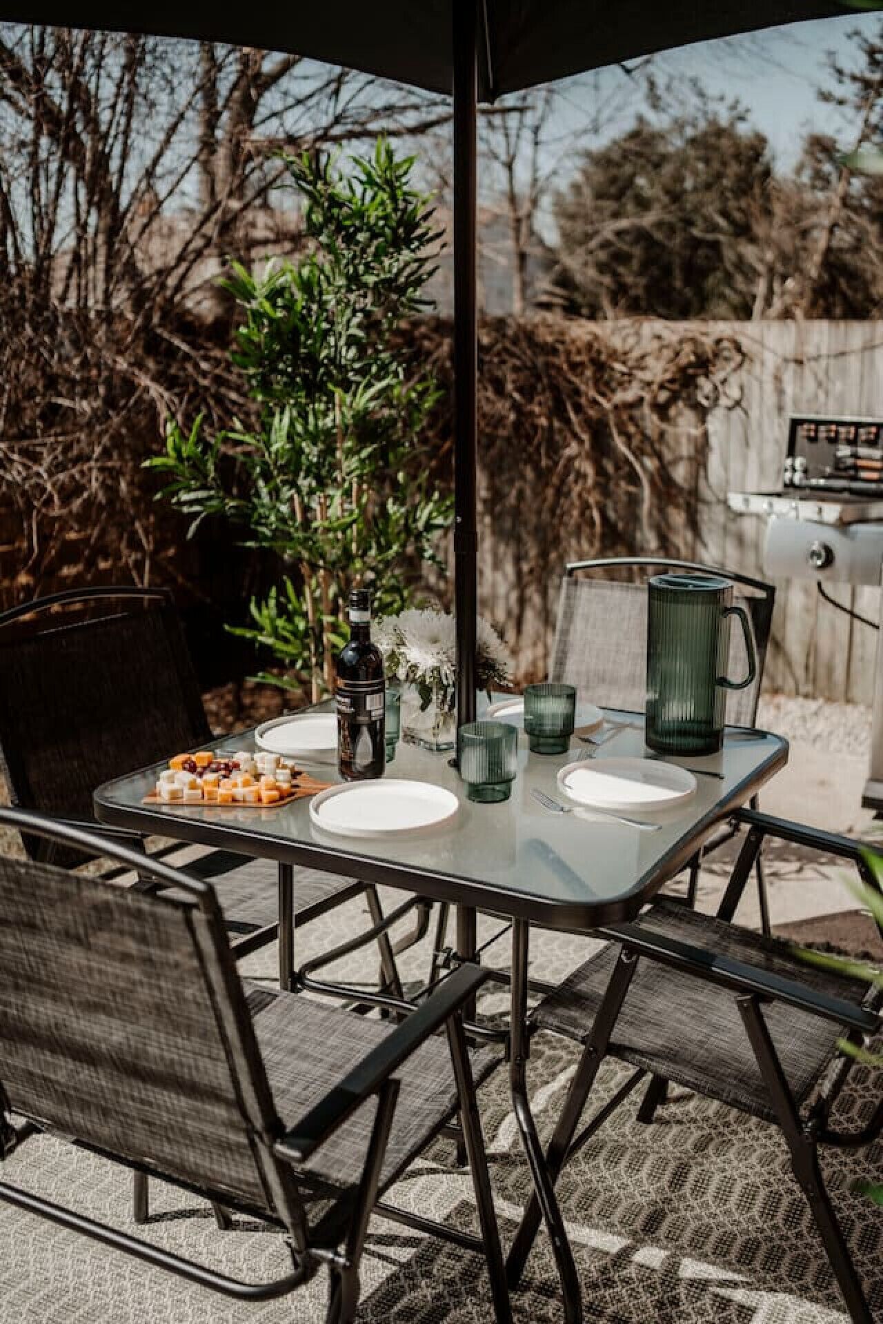 Un espace extérieur aménagé pour prendre les repas, avec une table en verre, des chaises en métal et une machine à café.