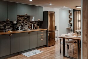 Une cuisine moderne avec des meubles de couleur sombre, un réfrigérateur en acier inoxydable et une table à manger en bois, préparée pour un repas à deux.
