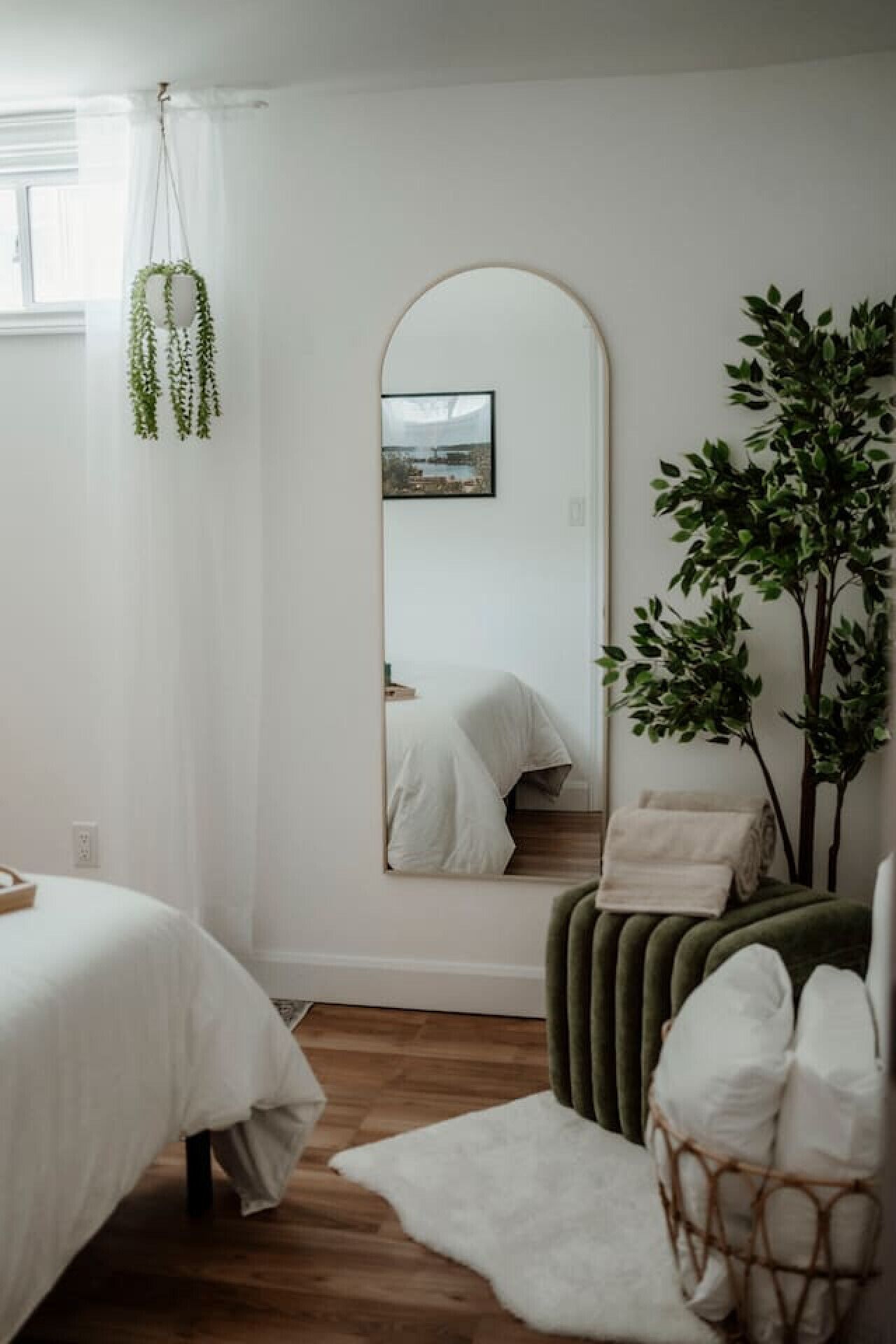 A bedroom with a large mirror, a bed, a green chair, and a white rug.