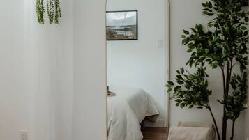 A bedroom with a large mirror, a bed, a green chair, and a white rug.