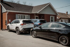 A residential street with two parked cars in front of a brick house.