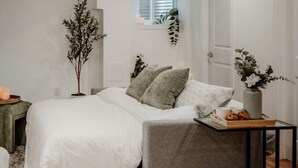 Een slaapkamer met een bed, nachtkastje, raam en een plant.