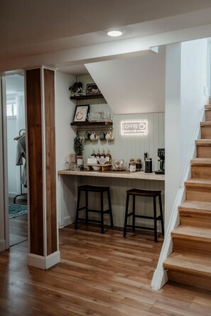 A compact kitchen with a wooden staircase, a coffee sign, and a small seating area.