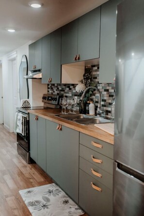A modern kitchen with grey cabinets, a wooden countertop, and a stainless steel refrigerator.