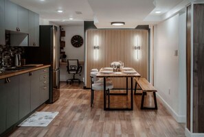 Een compacte keuken met moderne apparaten, een eethoek met een houten tafel en een bank, en een wandpaneel van hout.