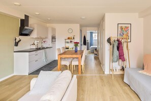 A modern apartment with a dining area, kitchenette, and a living room with a sofa and a bed.