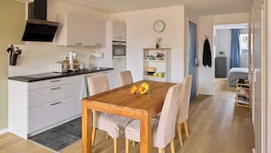 A compact kitchen with white cabinets, a black range hood, and a dining area with a wooden table and chairs. - Nimma Garden one bedroom apartment (Nijmegen)