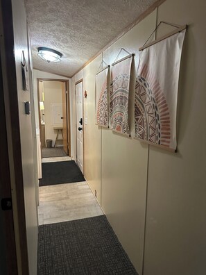 Un pasillo con piso alfombrado, una puerta al final y cortinas estampadas en la pared.
