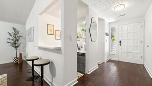 A hallway with dark wooden flooring, white walls, and a white door. There are two bar stools with round seats and black bases.
