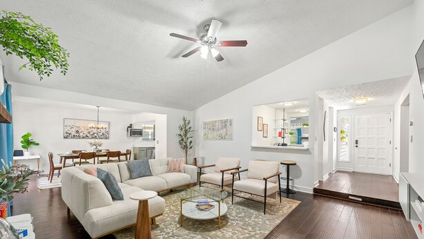 A spacious living room with a ceiling fan, a dining area, and a kitchen in the background.
