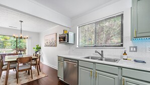 A modern kitchen with a dishwasher, a sink, and a window with blinds.