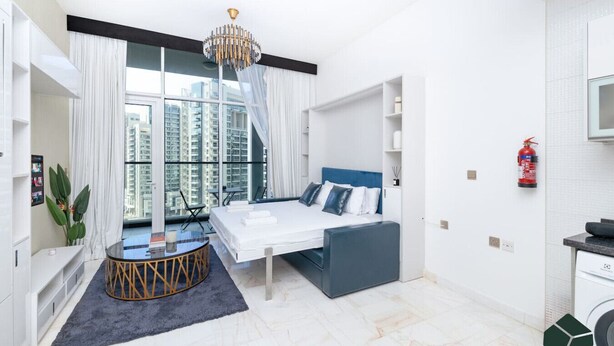 Ein modernes Hotelzimmer mit Bett, Schreibtisch, Sessel und einem großen Fenster mit Blick auf hohe Gebäude.