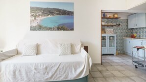 Ein Schlafzimmer mit Bett, Blick auf einen Strand und einer Küchenzeile mit Schränken und Spüle.