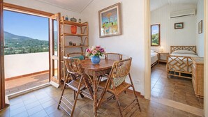 Ein Essbereich mit einem runden Holztisch, vier Bambusstühlen und einem Blumenstrauß. Eine Holzablage zeigt dekorative Gegenstände, und an der Wand hängt ein Gemälde.