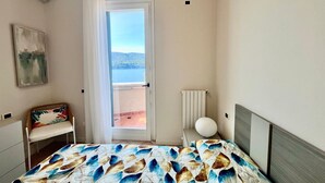 A bedroom with a bed, a chair, a radiator, and a view of the sea through a door. - La Pianotta suite with seaview (Porto Azzurro)