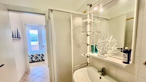 A modern bathroom with a white sink, a large mirror, and a shower area. - La Pianotta suite with seaview (Porto Azzurro)